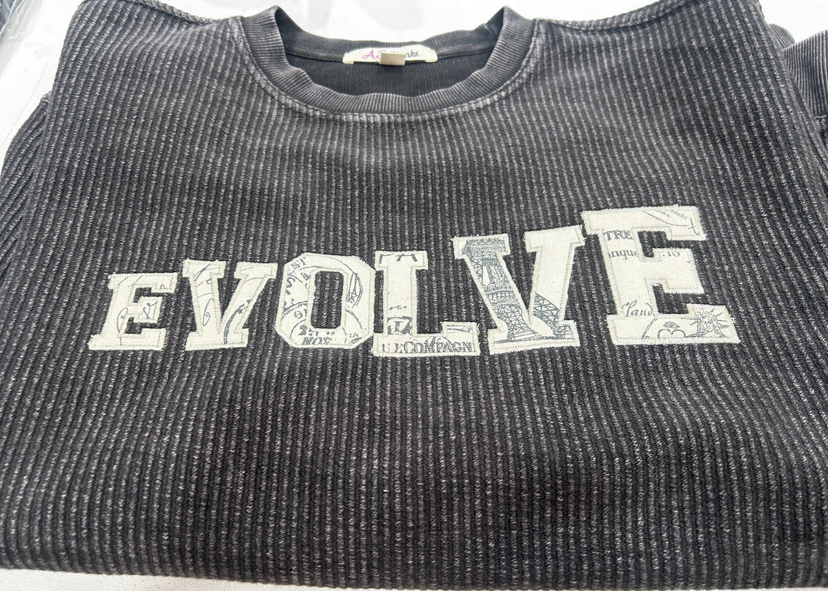 A close-up of a dark gray ribbed knit t-shirt featuring the word 'ENJOY' printed vertically in a distressed white collegiate font.