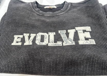 A close-up of a dark gray ribbed knit t-shirt featuring the word 'ENJOY' printed vertically in a distressed white collegiate font.