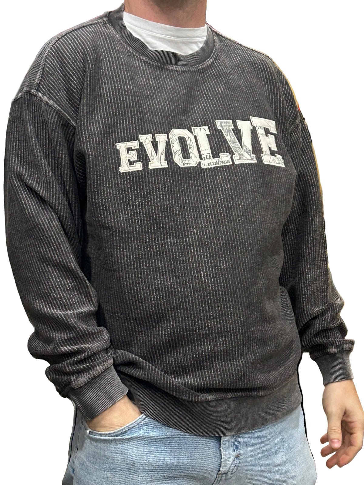 A man wearing a dark gray ribbed crewneck sweatshirt with 'EVOLVE' printed in white across the chest, paired with light blue jeans, standing in a retail or gym environment.