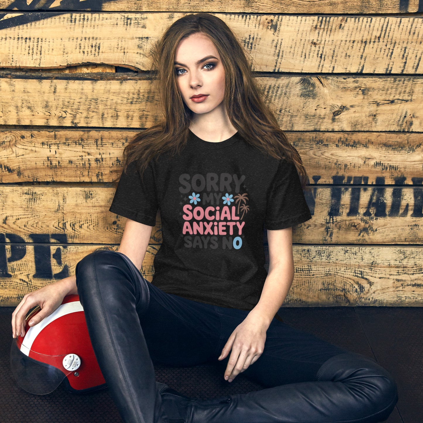 Person wearing a black t-shirt with colorful text, sitting against a wooden wall.