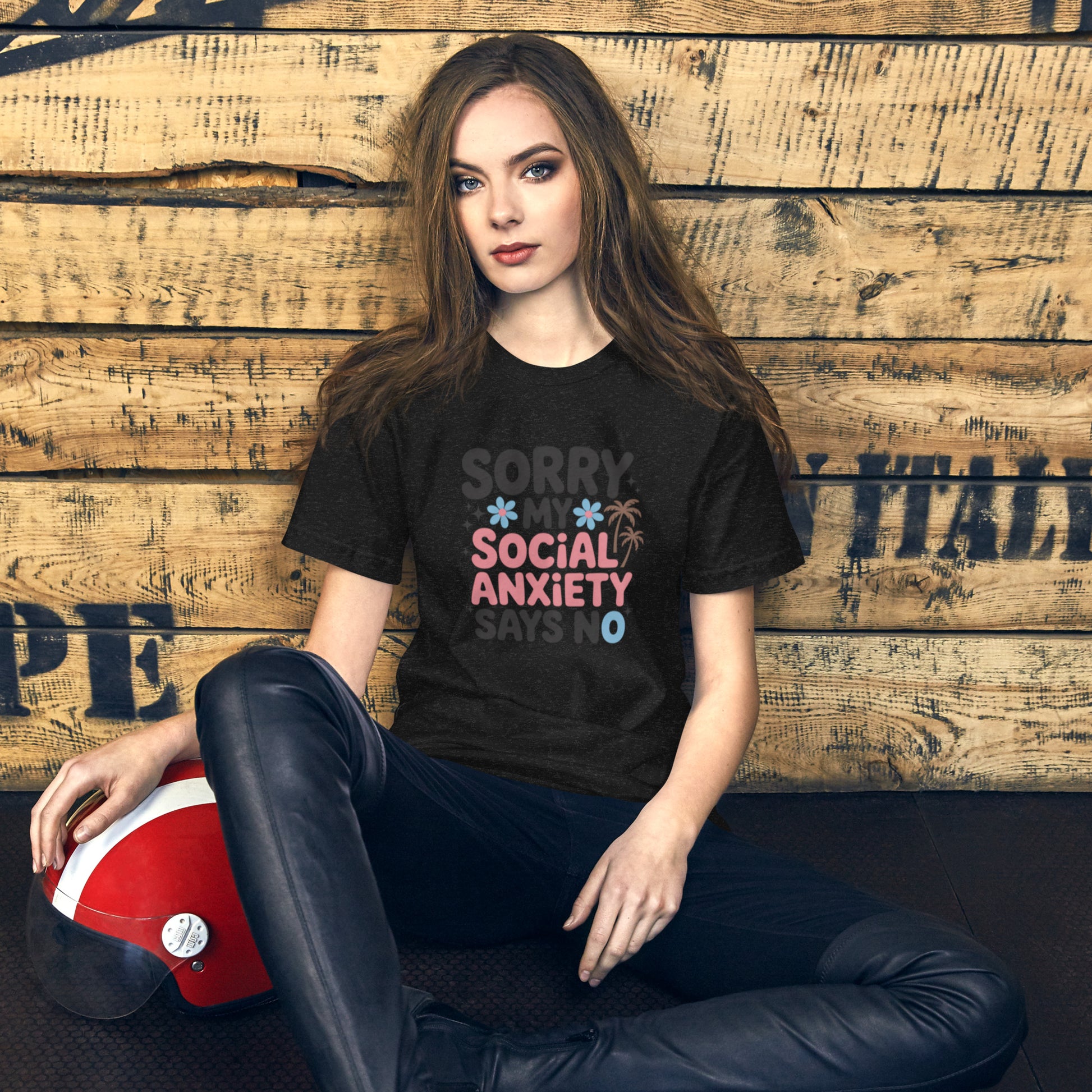 Person wearing a black t-shirt with colorful text, sitting against a wooden wall.