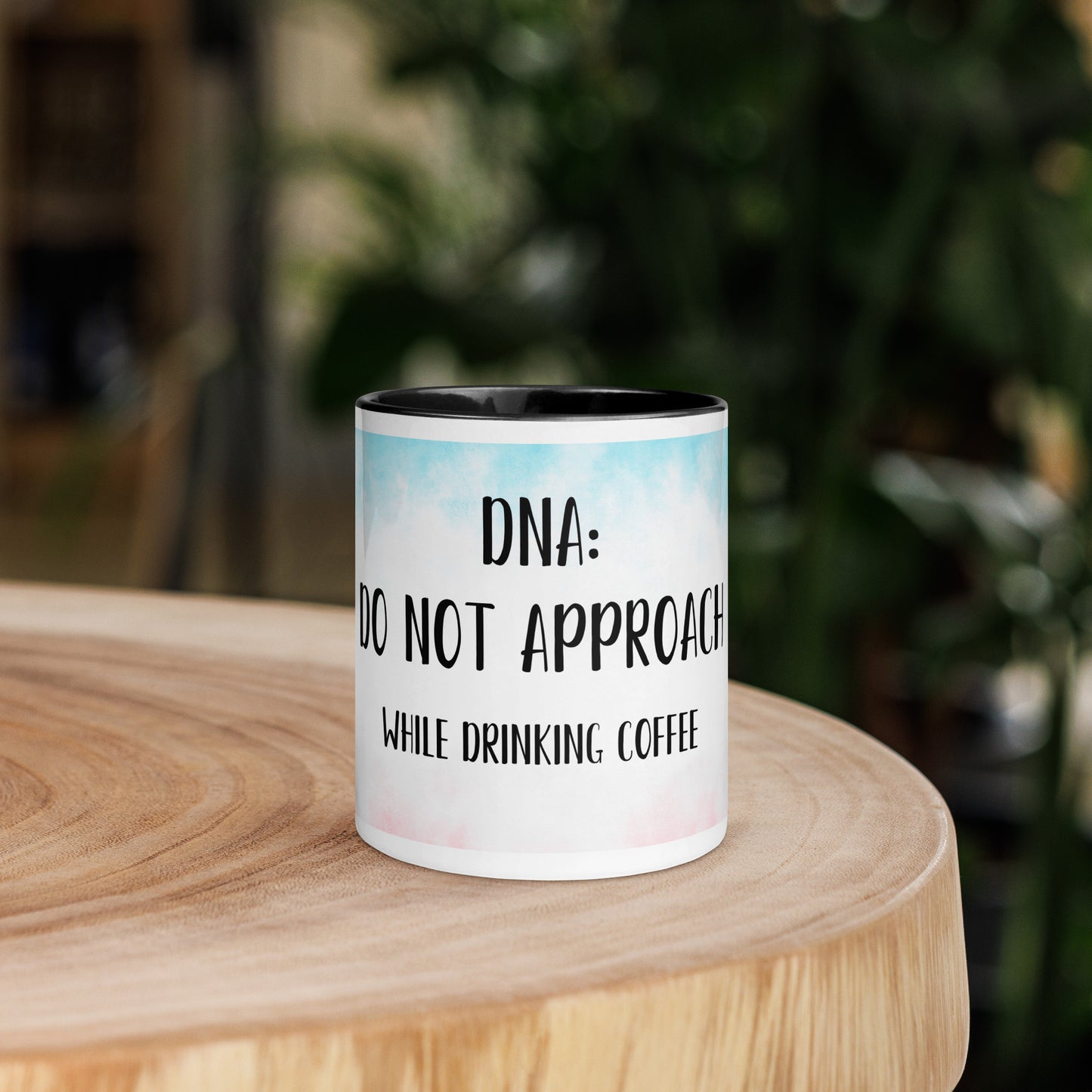 Mug with 'Do not approach while drinking coffee' text on a wooden surface with a blurred green background