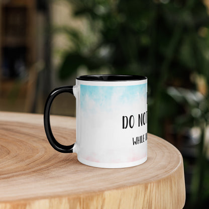 White 'coffee' mug with black handle and text on a wooden surface with a blurred green background 