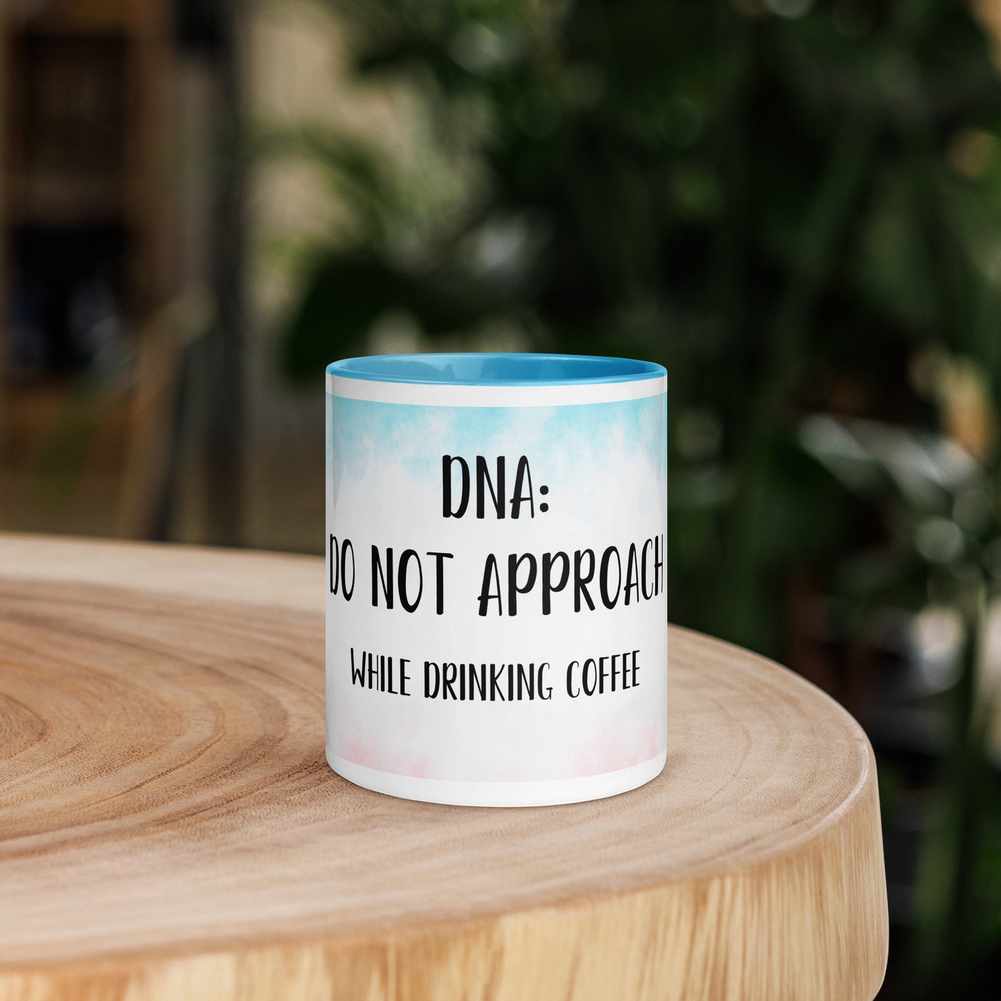 Mug with 'Do not approach while drinking coffee' text on a wooden surface with a blurred green background